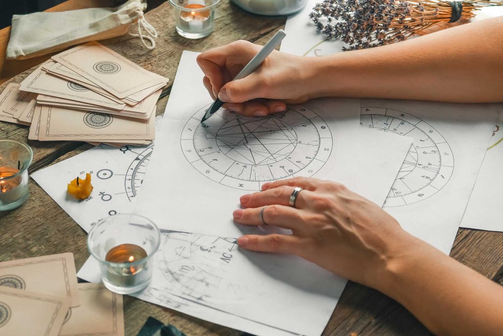 A person sketches a zodiac sign on paper, focusing intently on the intricate details of the drawing.