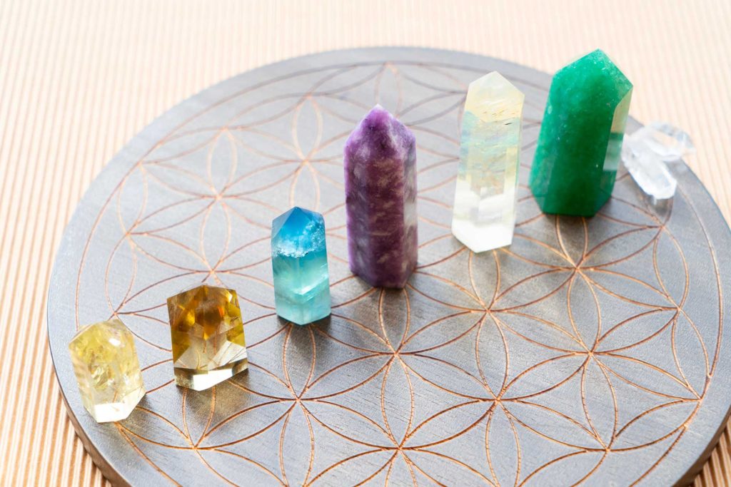 A wooden tray holds a clear crystal and three colored crystals: red, blue, and green, arranged neatly.