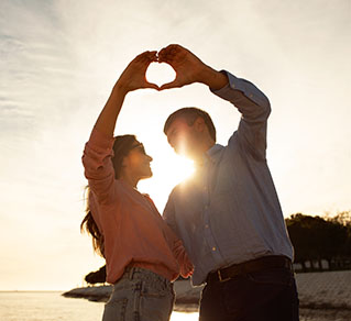 Couple on the beach forming a heart shape with their hands, symbolizing love and connection.