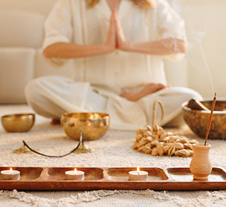 A woman meditates peacefully in a softly lit room, surrounded by a tray of flickering candles.