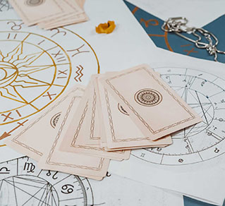 A spread of tarot cards resting on astrological charts and papers, with a decorative chain and a yellow flower petal nearby.