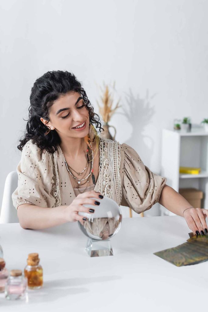 A woman sits at a table, gazing intently into a crystal ball, surrounded by mystical decor.